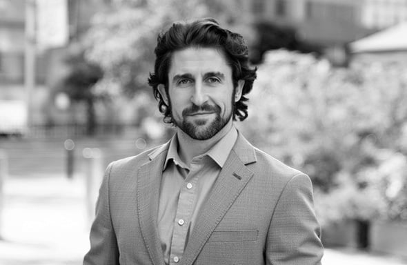 Black and white image of man in suit standing in front of cityscape